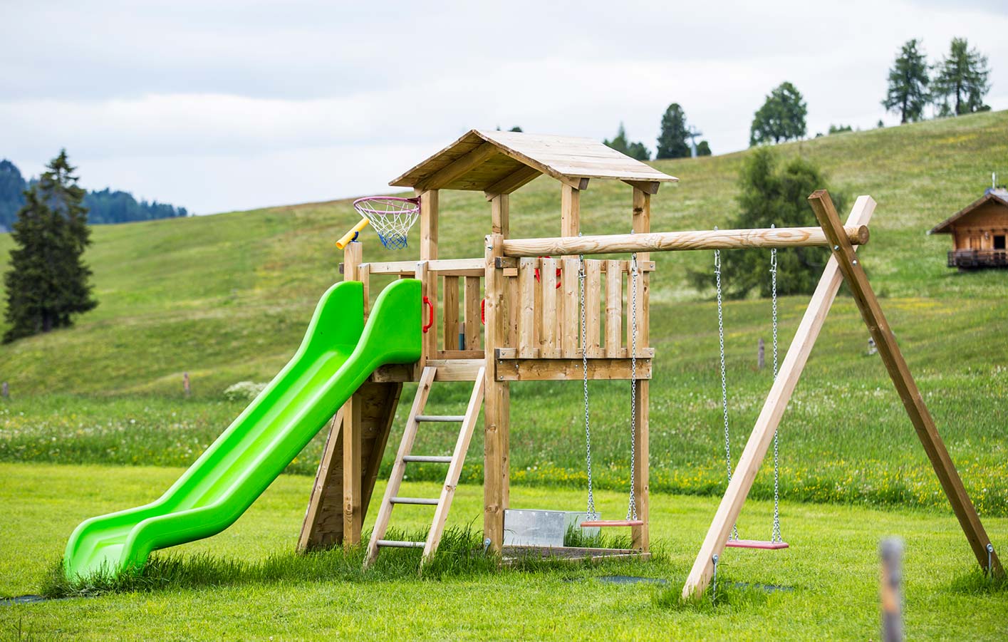 Ein Spielturm aus Holz mit Rutsche und Schaukel auf einer Wiese